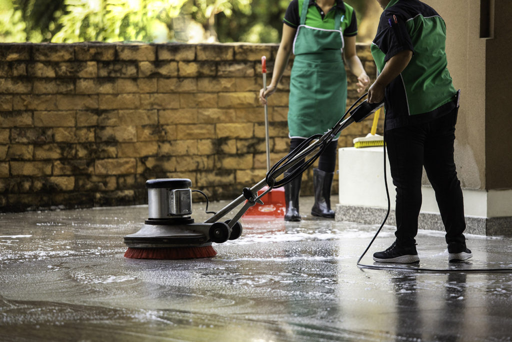Worker cleaning floor exterior walkway using polishing machine